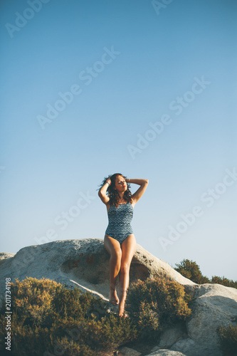 Pretty young woman sitting on the rocky shore by the sea