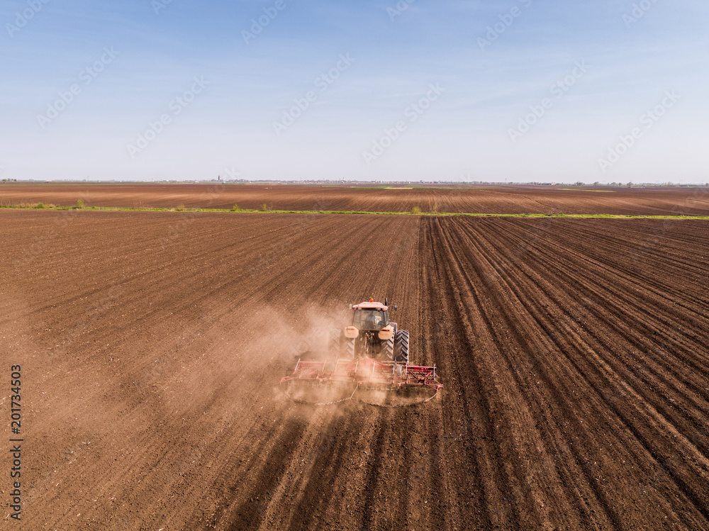 Obraz premium Aerial shot of a tractor cultivating field at spring
