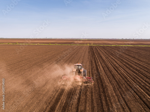Aerial shot of a tractor cultivating field at spring
