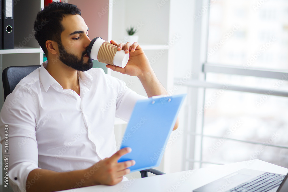 Young handsome entrepreneur sitting at desk and using laptop in office. Young handsome entrepreneur sitting at desk and using laptop in office.