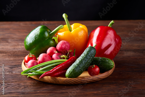 Wooden plate with vegetables for a vegetarian salad on rustic wooden background  close-up  selective focus