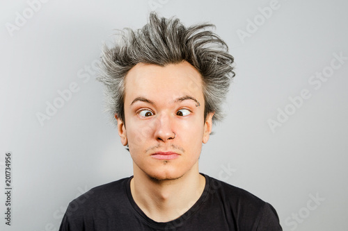 Unshorn and unshaven squint young guy with piercings on his face on gray background.