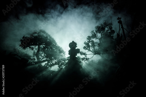 Horror Halloween decorated conceptual image. Alone girl with the light in the forest at night. Silhouette of girl standing between trees with surreal light . Selective focus.