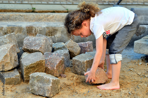 Kind hebt schweren Stein auf Baustelle