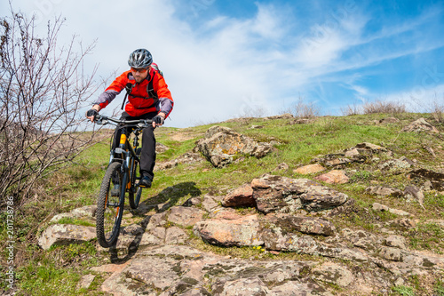 Cyclist in Red Jacket Riding Mountain Bike Down Rocky Hill. Extreme Sport and Adventure Concept.