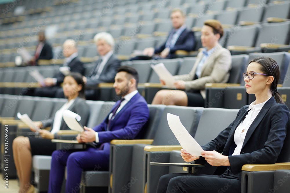 © pressmaster - Group of delegates with documents listening attentively to speaker by tribune at business or political conference