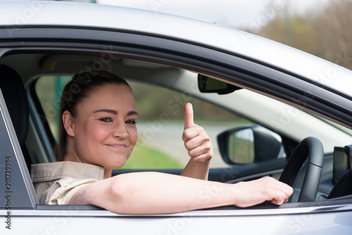 Beautiful young woman driving her brand new car and showing her thumb up