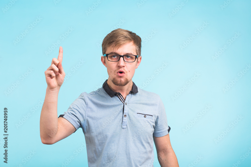 Fototapeta premium Wow, I understand it. Surprised young male raises finger as remembers something, isolated over blue background. Reaction and people