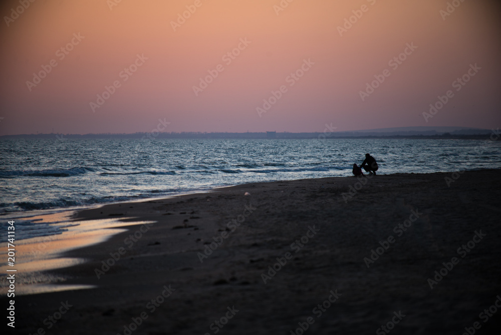 father and son sit near the sea at sunset