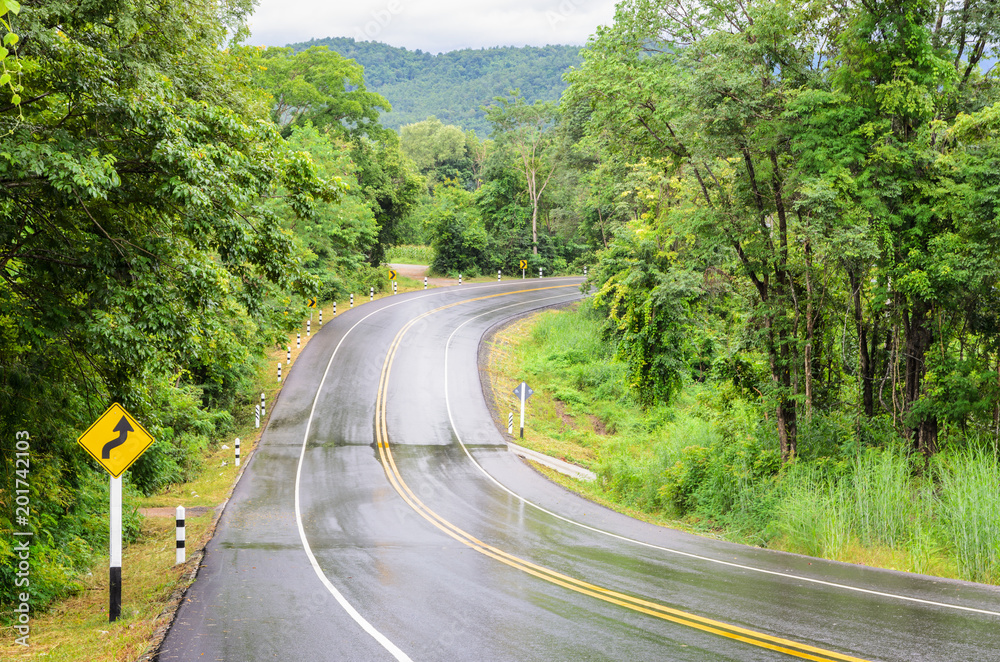 Wet mountain asphalt road after rain with traffic sign of sharp reverse curves ahead sign