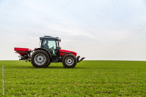 Farmer in tractor fertilizing wheat field at spring with npk