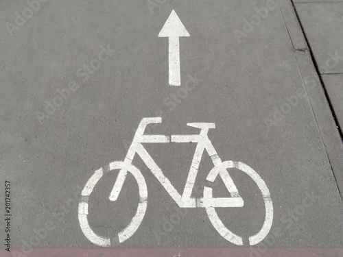 White bicycle symbol on the street and direction of movement. Bicycle road sign and white arrow on asphalt