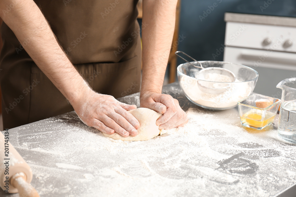 Man kneading dough on table covered with flour in kitchen Man kneading dough on table covered with flour in kitchen