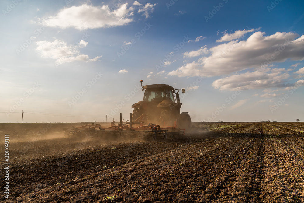 Fototapeta premium Tractor cultivating field at spring