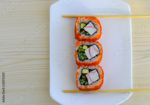 Sushi a dish of traditional Japanese cuisine cooked from rice, calves of a salmon, crabmeat, avocado and a cucumber. Sushi are on a white plate. Wooden sticks hold sushi photo