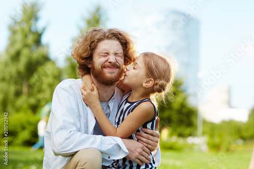 Funny young bearded man embracing his cute little daughter while spending summer day with her