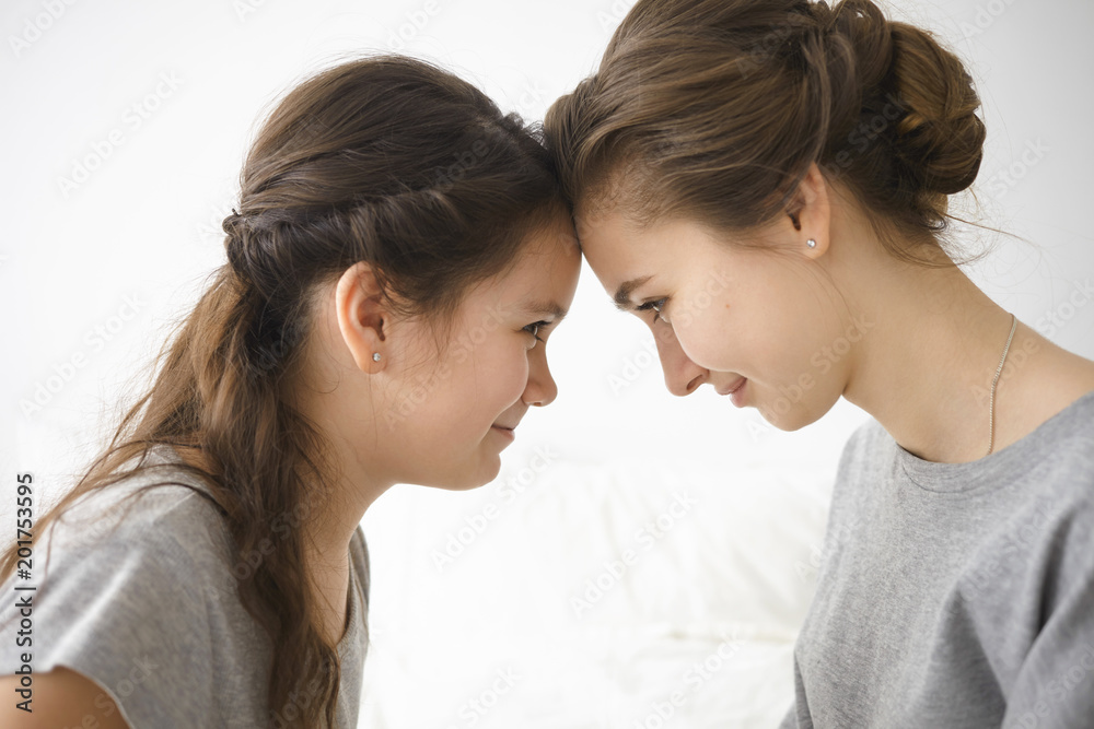 Sideways shot of happy young Caucasian mother and her little daughter spending morning together at home, posing with their foreheads against each other, smiling joyfully. Family bonding and love Sideways shot of happy young Caucasian mother and her little daughter spending morning together at home, posing with their foreheads against each other, smiling joyfully. Family bonding and love