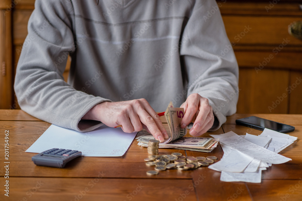 Close up man with calculator counting, making notes at home, hand is writes in a notebook. Stacked coins arranged at deesk. Savings finances concept. Close up man with calculator counting, making notes at home, hand is writes in a notebook. Stacked coins arranged at deesk. Savings finances concept.