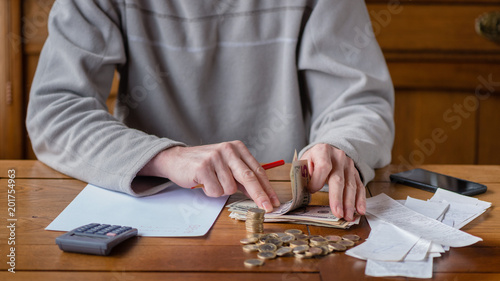Close up man with calculator counting, making notes at home, hand is writes in a notebook. Stacked coins arranged at deesk. Savings finances concept.