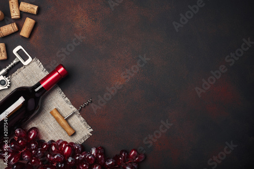 Bottle of wine, red grapes, corkscrew and corks, on rusty background top view
