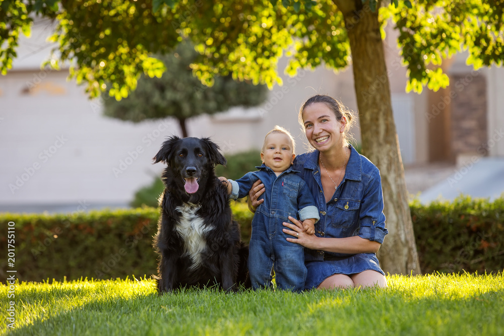 A mother with baby son and black dog in green neighborhood