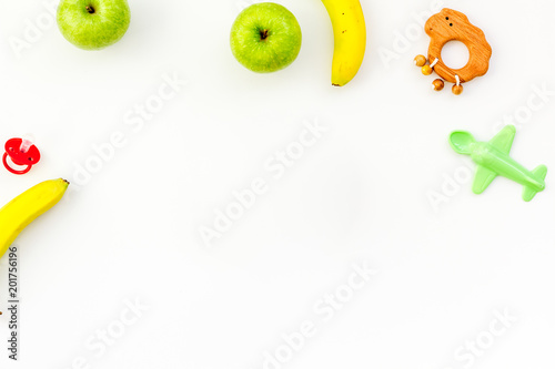 Healthy nutrition for babies. Apple, banana near toys on white background top view copy space