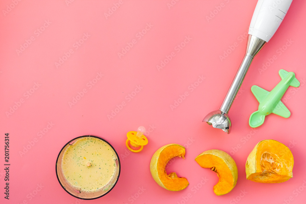 Make baby food at home. Puree with pumpkin near immersion blender, pacifier, toy on pink background top view copy space Make baby food at home. Puree with pumpkin near immersion blender, pacifier, toy on pink background top view copy space