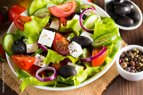 Fresh Greek salad made of cherry tomato, ruccola, arugula, feta, olives, cucumbers, onion and spices. Caesar salad in a white bowl on wooden background. Healthy organic diet food concept.