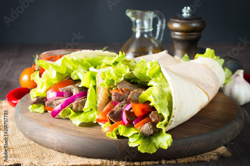 Photo of Mexican sandwich food, burrito, fajita, tacos, wrap made of tortilla, beef, chicken, fresh vegetables on rustic wooden background. Fast food concept. Healthy lunch snack. Copy space. 