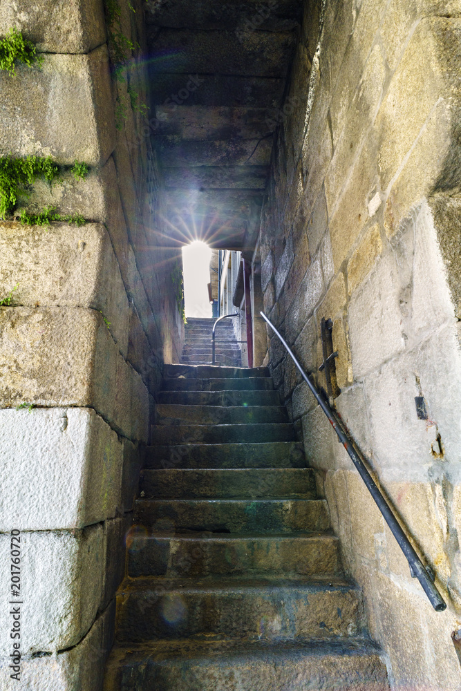 Backlight with sun reflections on ancient stone stairs under a tunnel in a narrow passageway next to the banks of the Douro river estuary in Porto, Portugal