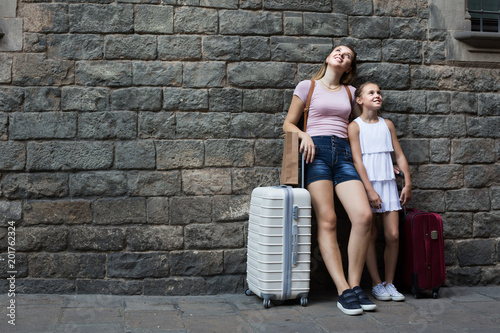 Woman and daughter standing with suitcases on stone wall