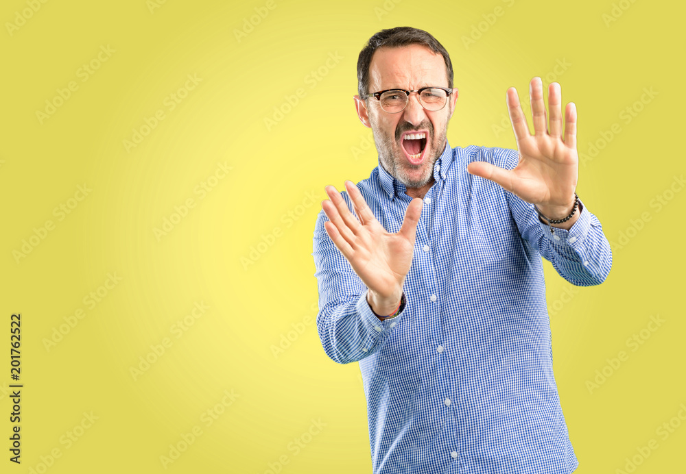 Handsome middle age man disgusted and angry, keeping hands in stop gesture, as a defense, shouting Handsome middle age man disgusted and angry, keeping hands in stop gesture, as a defense, shouting