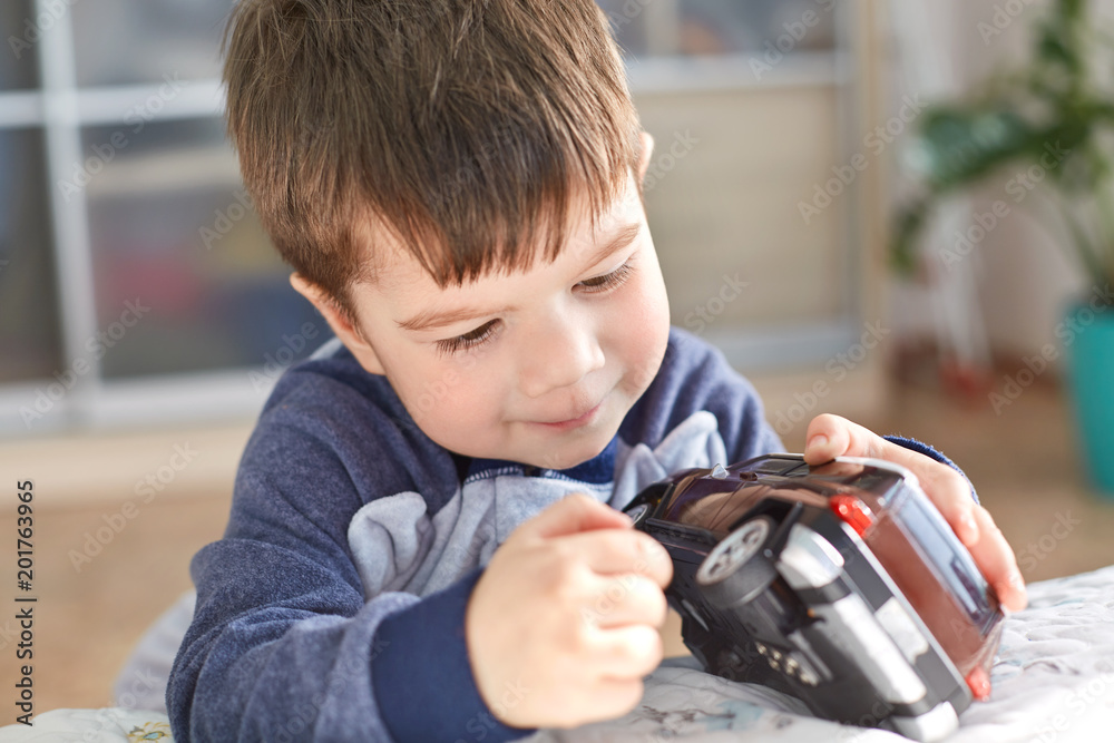 Indoor shot of good looking small kid holds toy car in hands, poses indoor against cozy domestic interior, likes to play with toys, has appealing look. Joyful cute boy preschooler being naughty Indoor shot of good looking small kid holds toy car in hands, poses indoor against cozy domestic interior, likes to play with toys, has appealing look. Joyful cute boy preschooler being naughty