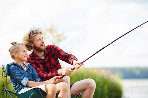 Two friendly guys pulling rod while fishing on summer weekend in natural environment