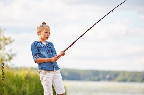 Young boy with rod standing by lake and waiting for huge fish to catch