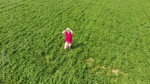 A woman in a red T-shirt poses in front of the drony camera. He runs away from the camera and runs after her. Fun and sports on a wheat field photo