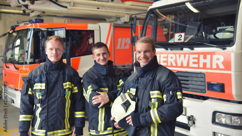 Portrait einer Gruppe Feuerwehrmänner vor den Einsatzfahrzeugen auf der Feuerwache // Portrait of a group of firefighters in front of the fire station vehicles