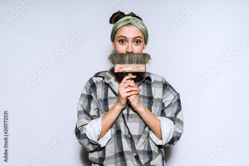 cute young girl in a plaid shirt holding a large brush, doing repairs in the apartment