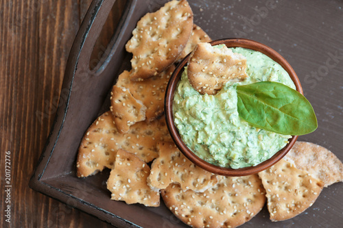 Bowl with tasty spinach sauce and crackers on wooden tray