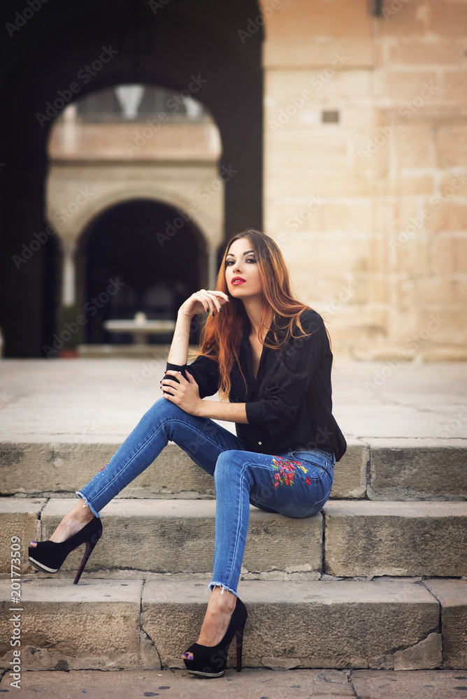 beauty girl dressed in denim and black shirt with orange hair in street sitting on a stone stairs beauty girl dressed in denim and black shirt with orange hair in street sitting on a stone stairs