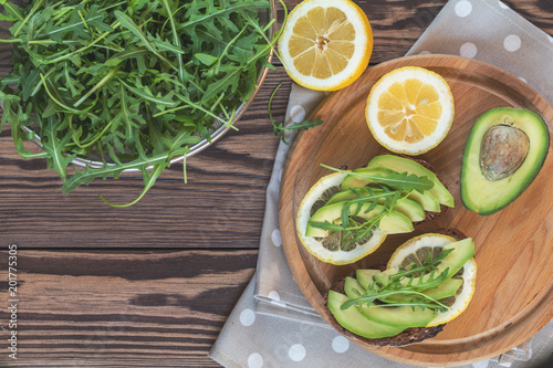 Rye bread with cut avocado, arugula and lemon on round board