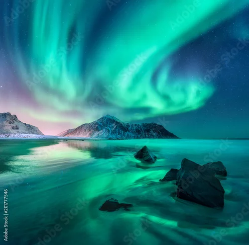 Obraz Zorza polarna. Zorza polarna na Lofotach, Norwegia. Niebo z polarnymi światłami, gwiazdami. Noc zimowy krajobraz z zorzą polarną, morze z odbiciem nieba, kamienie, piaszczysta plaża i góry. Zielona zorza polarna