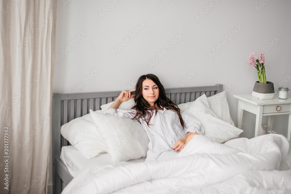 sexy young brunette woman wearing a white shirt on the bed at home. Girl's morning sexy young brunette woman wearing a white shirt on the bed at home. Girl's morning