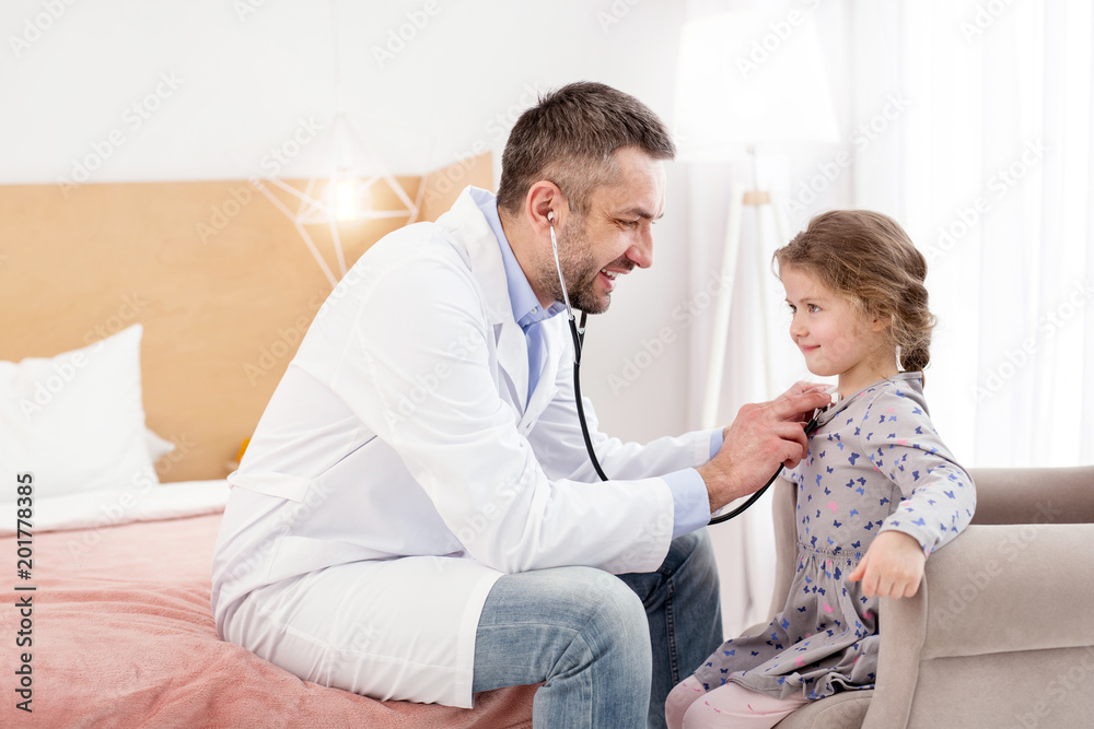 Fototapeta premium Good rhythm. Exuberant experienced doctor examining his patient and listening to the girls heartbeat