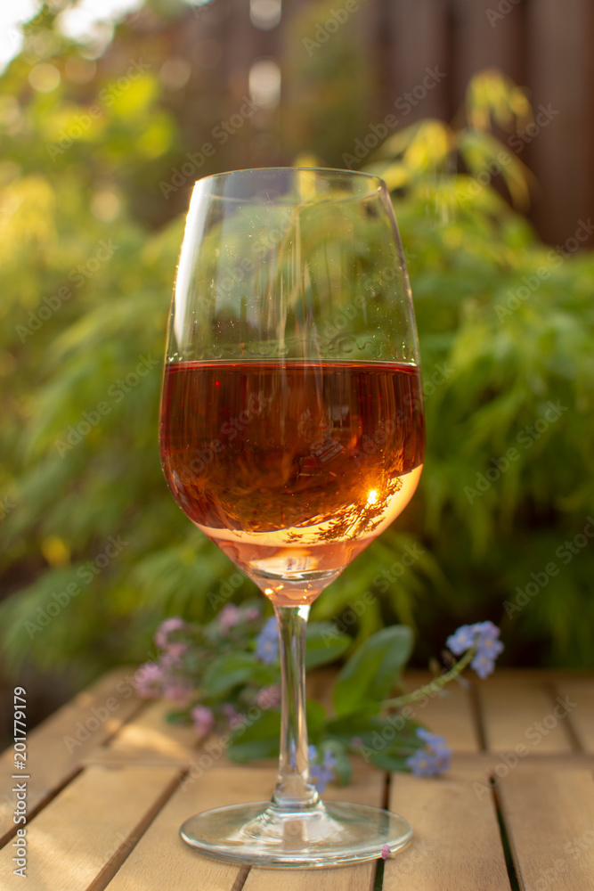 One cold rose wine glass served on outdoor terrace in garden with flowers