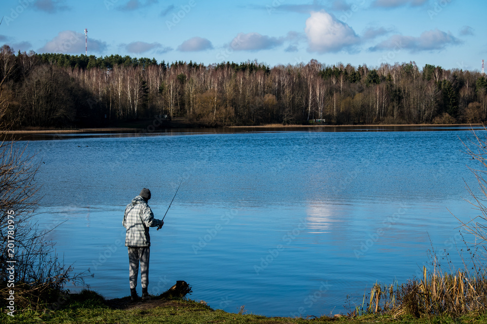 Man fishing rod on the shore of the pond in the woods