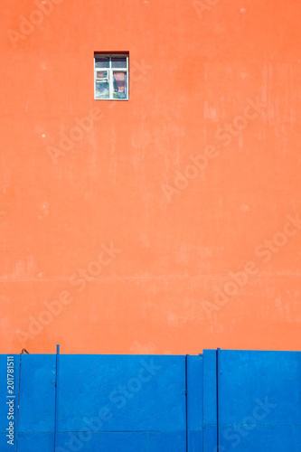 Orange wall of a house with one window Contrast with a blue fence. Back background Texture photo