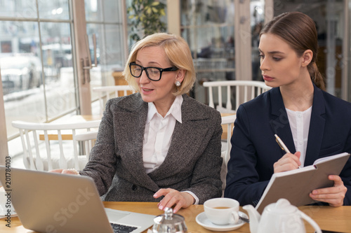 My apprentice. Unsmiling young woman discussing business with her employer while having tea