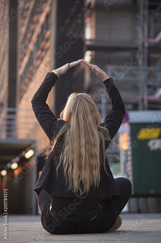 Mujer sentada delante de un edificio en obras haciendo el signo de casa con sus manos.