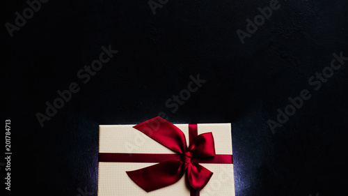 luxury stylish present on dark background. soft cream gift box with ruby red ribbon bow. elegant and exclusive reward on birthday or valentines day. free space concept